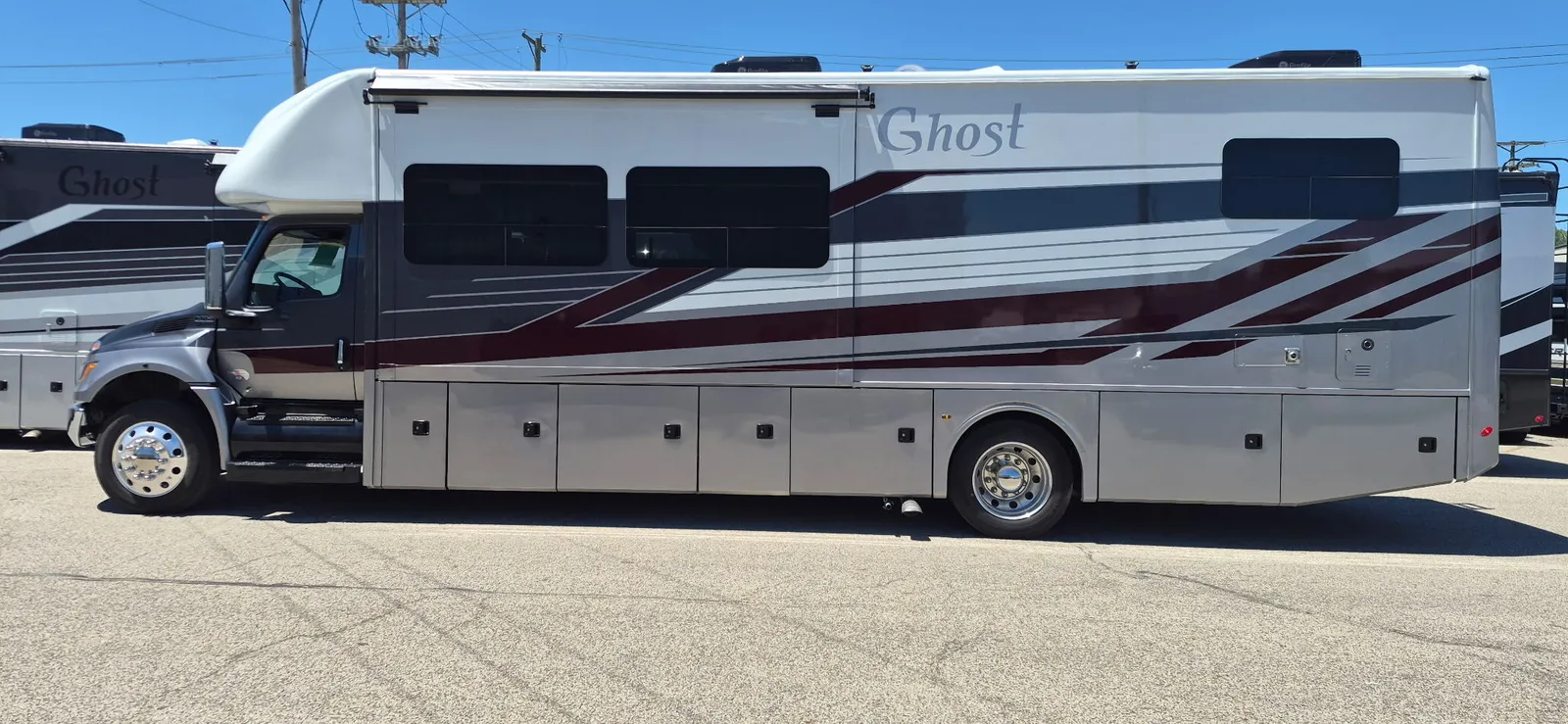 2027 Nexus Ghost 36DS Super C motorhome, side view of white motorhome with burgundy stripe and storage compartments