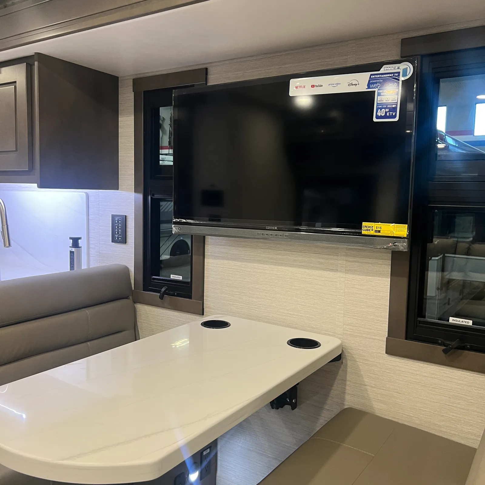 2027 Dynamax Corp DX3 32KD Super C motorhome, living area with dinette, large flatscreen tv, and kitchenette
