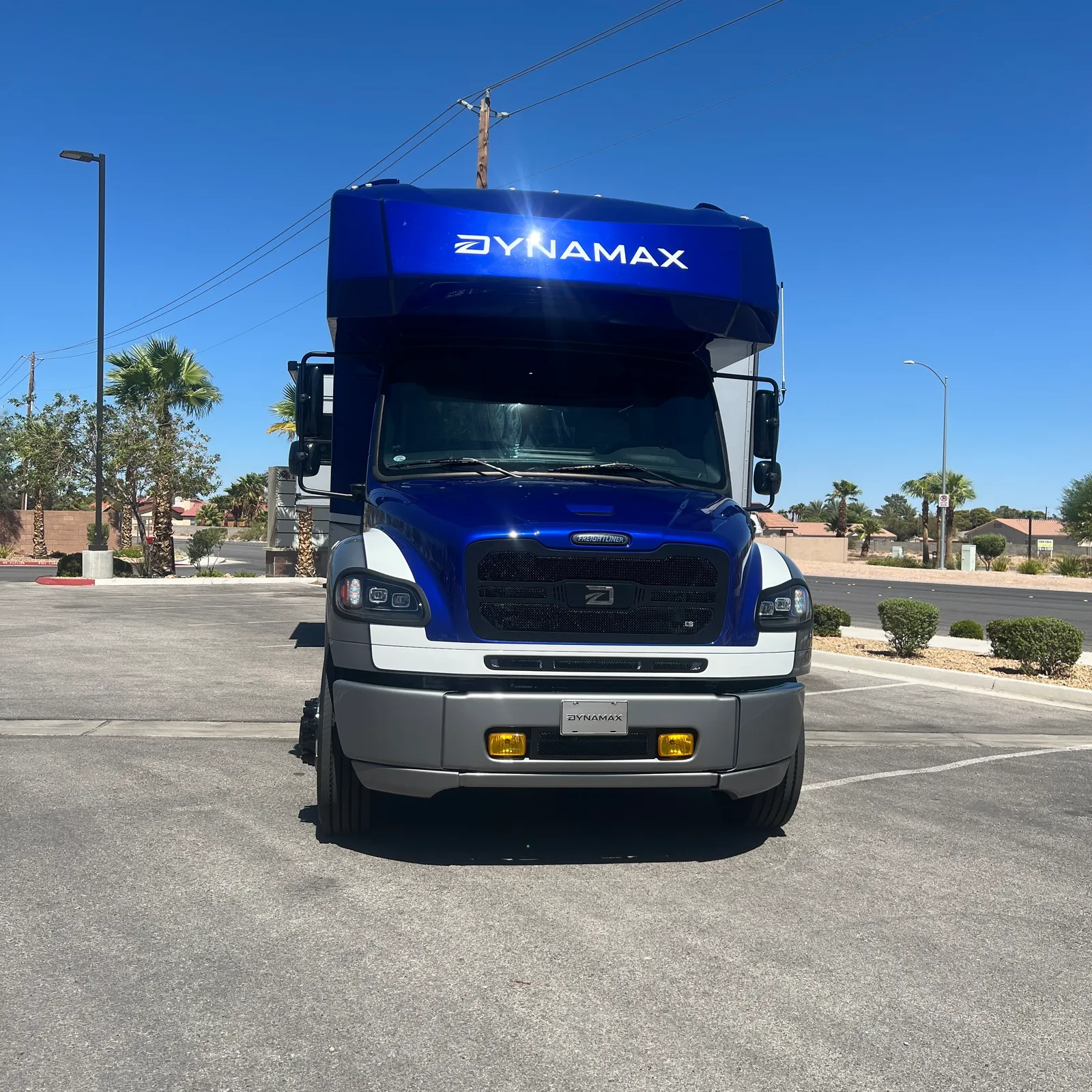 2027 Dynamax Corp DX3 32KD Super C motorhome, blue and white motorhome front view with desert landscape background