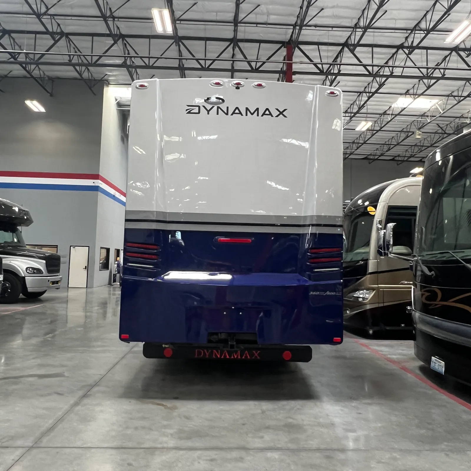 2027 Dynamax Corp Europa S 37CA Super C motorhome, rear view of white and dark blue motorhome in dealer showroom