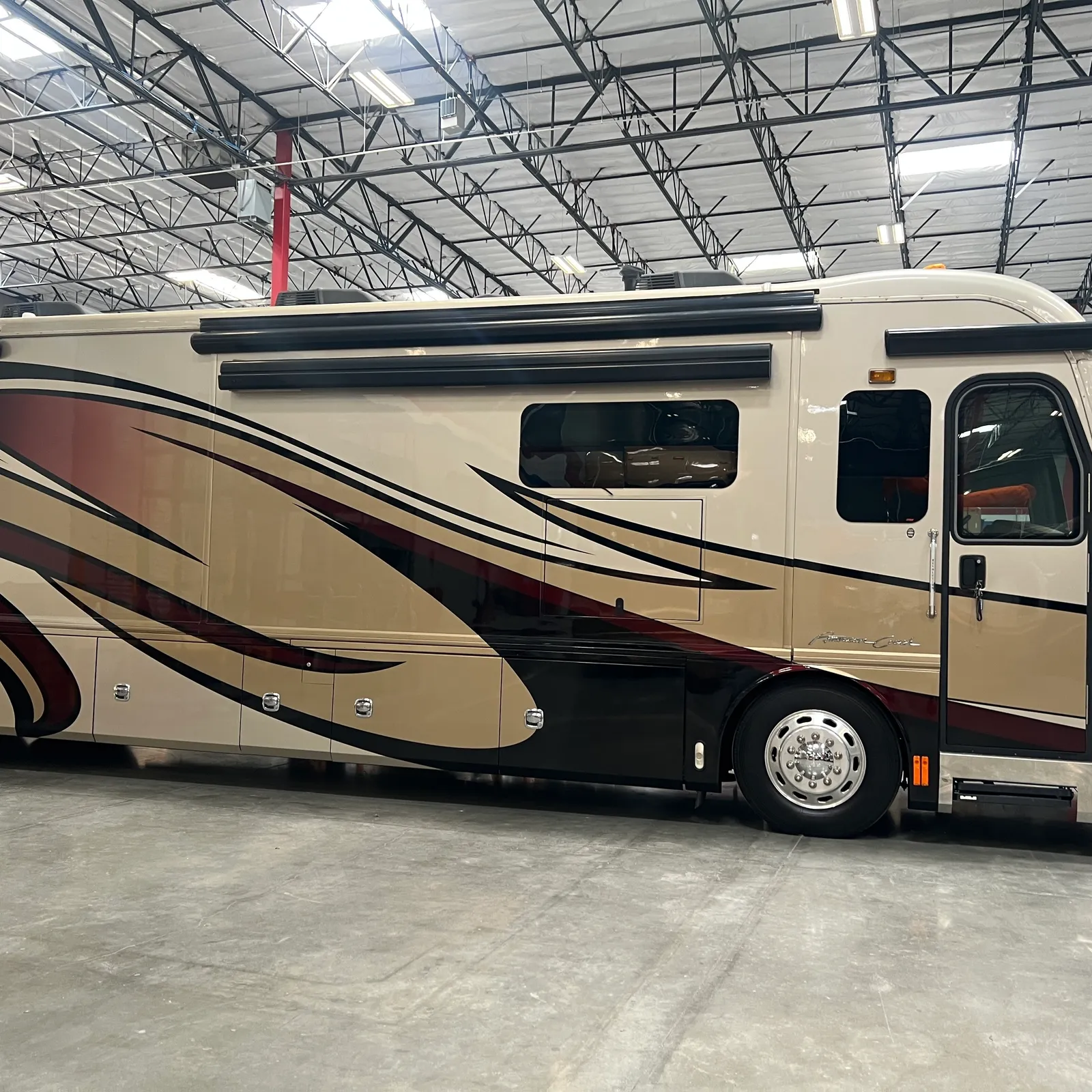 2013 American Coach American Revolution 42T Class A Diesel Pusher motorhome, cream and burgundy motorhome with curved graphic stripe in indoor storage facility