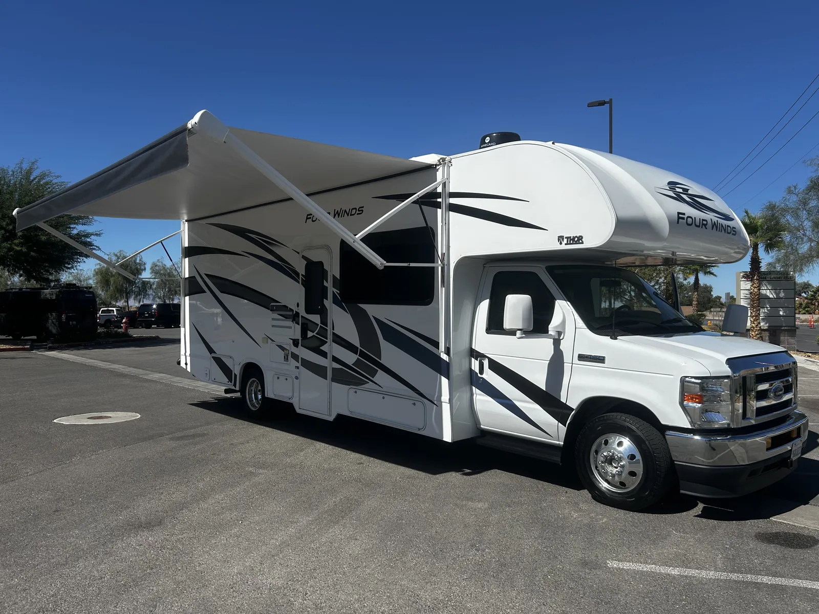 2023 Thor Motor Coach Four Winds Super C motorhome, white and gray motorhome with extended awning in parking lot