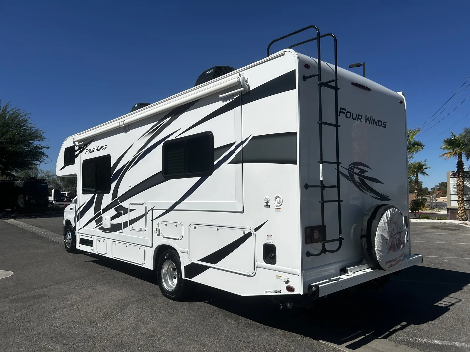 2023 Thor Motor Coach Four Winds Super C motorhome, white and black motorhome with awning and ladder on clear day