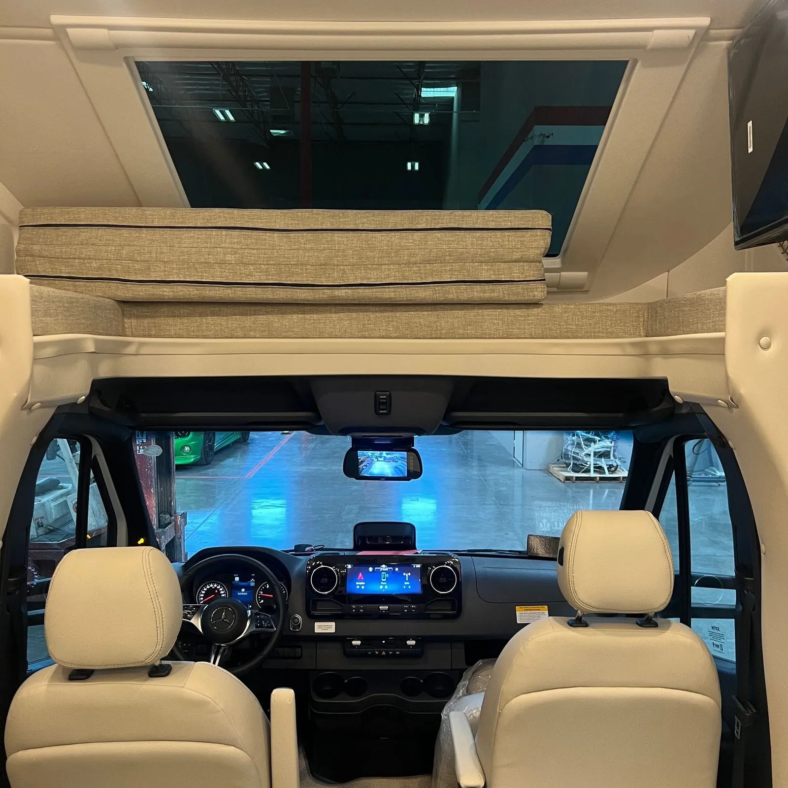 2026 Thor Delano 24XL Class C motorhome, driver's area with steering wheel, dashboard, touchscreen display, and cream-colored seats
