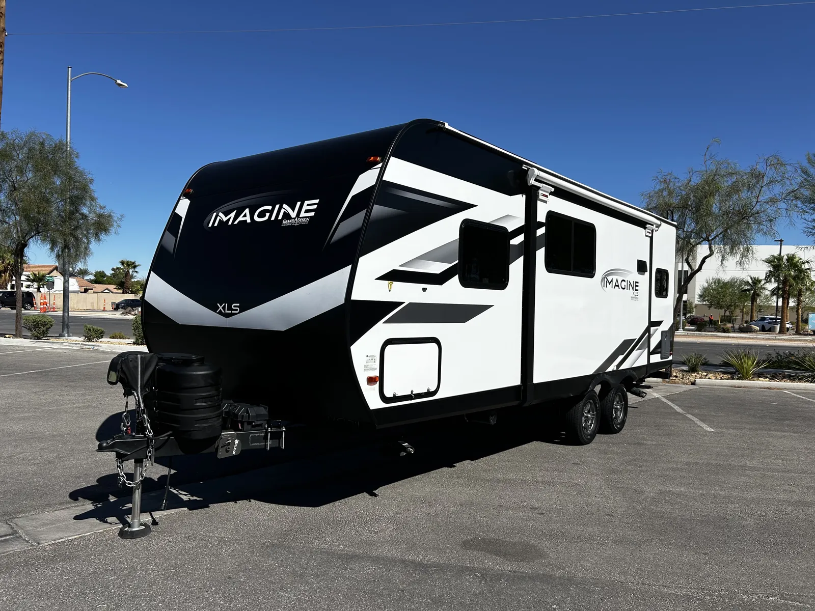 2024 Grand Design Imagine Xls 22MLE Travel Trailer motorhome, black and white travel trailer with extended awning on parking lot