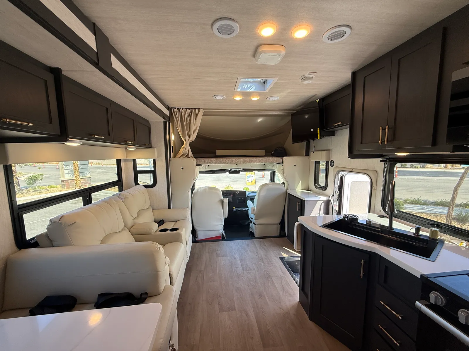 2027 Nexus Ghost 36DS Super C motorhome, living area with cream sofa, kitchen, and cockpit seating forward