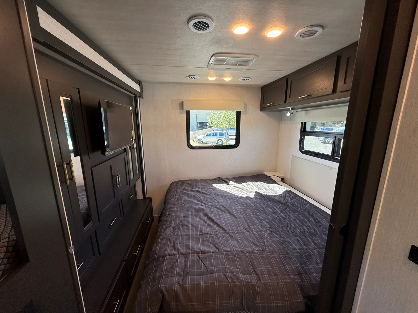 2027 Nexus Ghost 36DS Super C motorhome, bedroom with queen bed, dark cabinetry, and windows with bedside lights