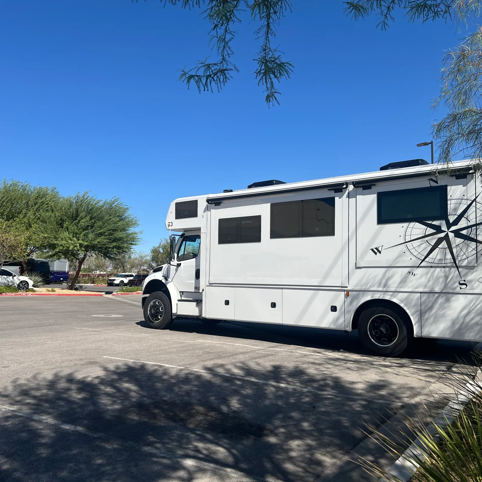 2027 Dynamax Corp Europa 31SS Super C motorhome, white motorhome parked in sunny lot with trees and landscaping